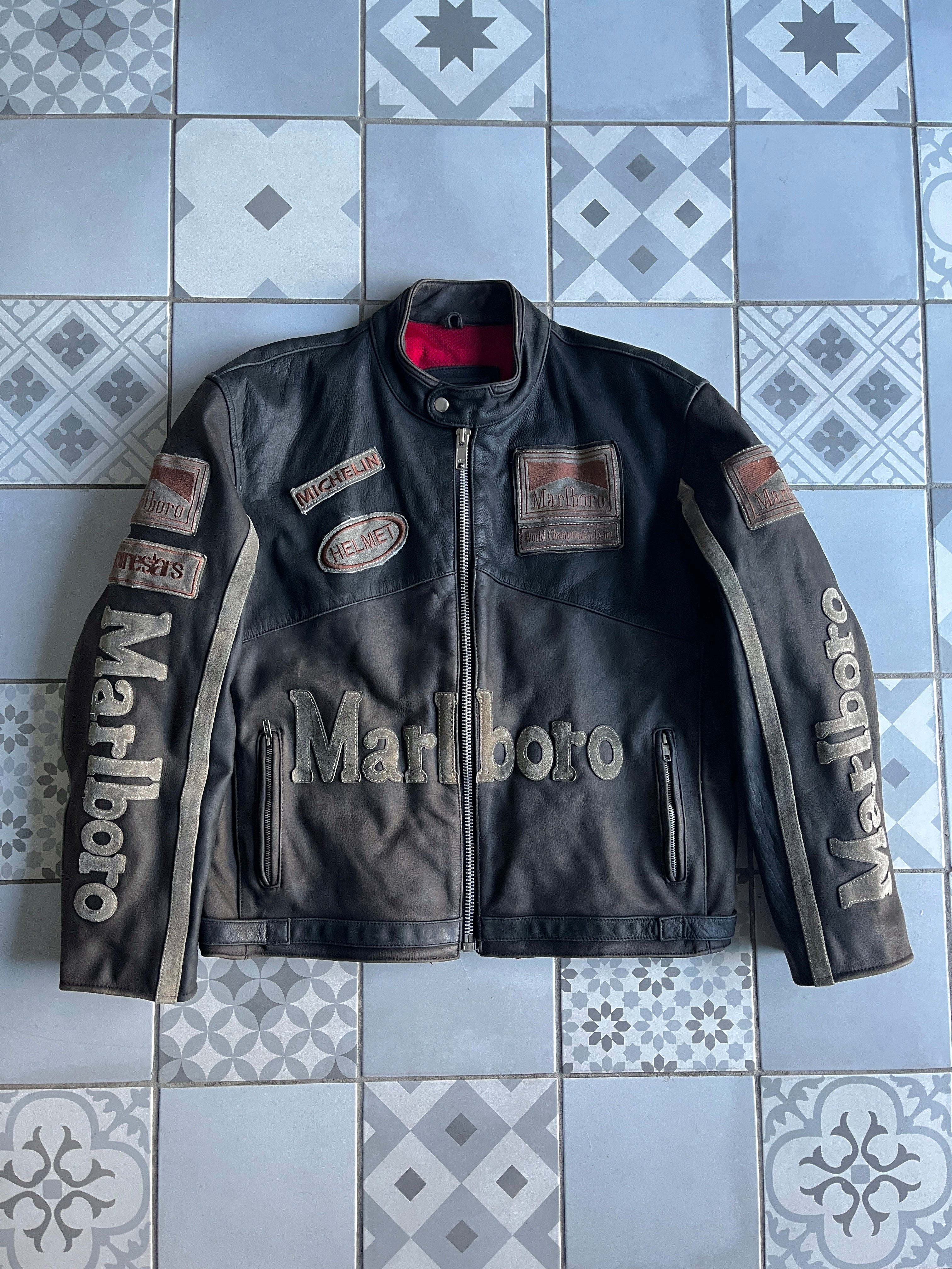 Vue de face du blouson cuir vintage Marlboro Racing noir patiné, avec logos brodés Michelin, Alpinestars et lettrage Marlboro sur la taille.