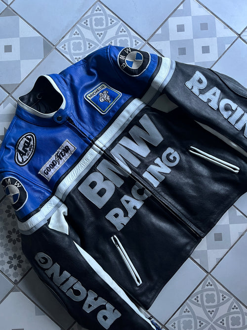 Vue de face complète du blouson moto vintage BMW Racing en cuir bleu et noir, avec logos sponsors Michelin, Goodyear, Arai et lettrage RACING sur les manches.