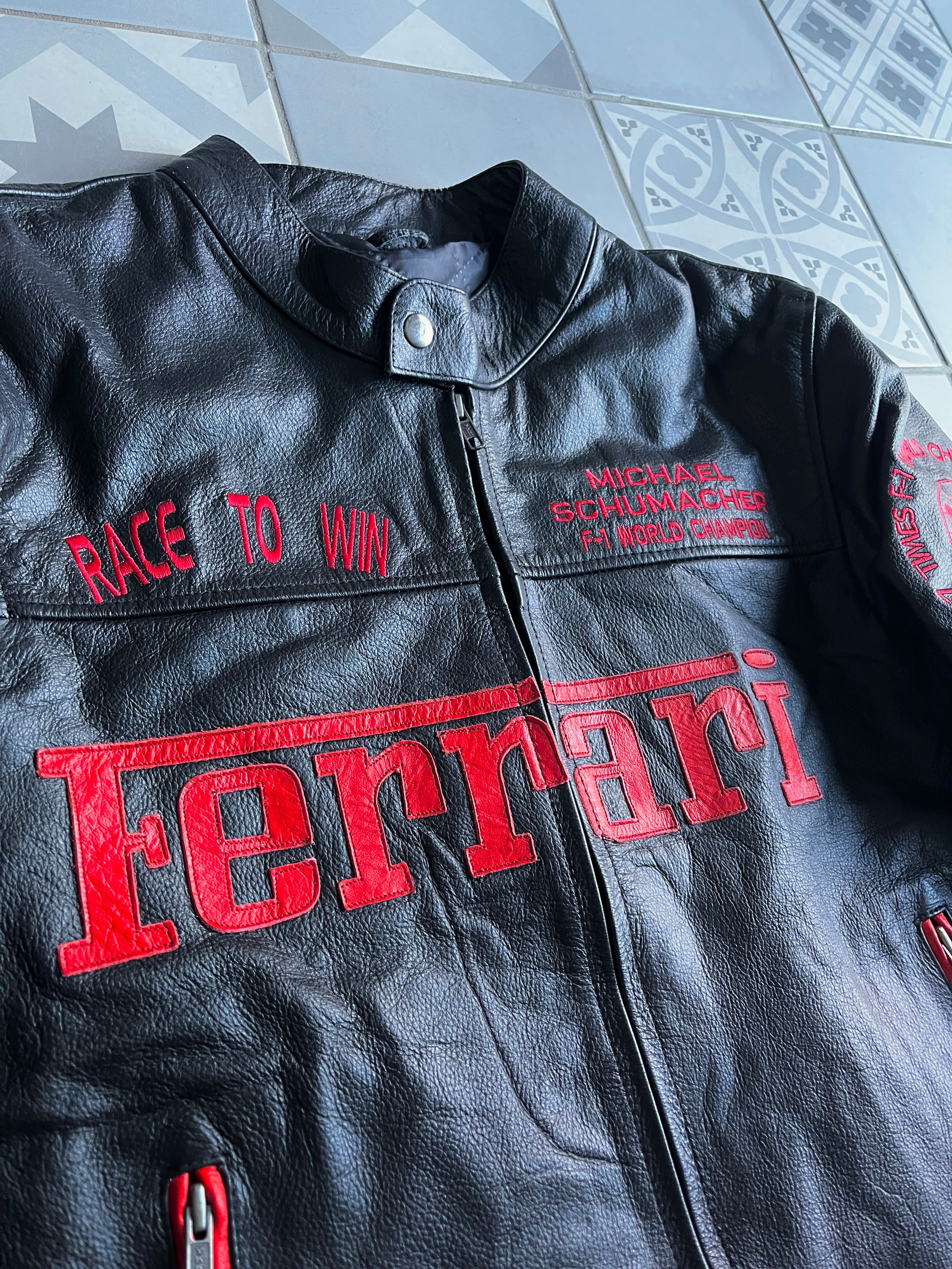 Gros plan sur les broderies 'Michael Schumacher F-1 World Champion' et 'Race to Win' sur la poitrine du blouson en cuir.