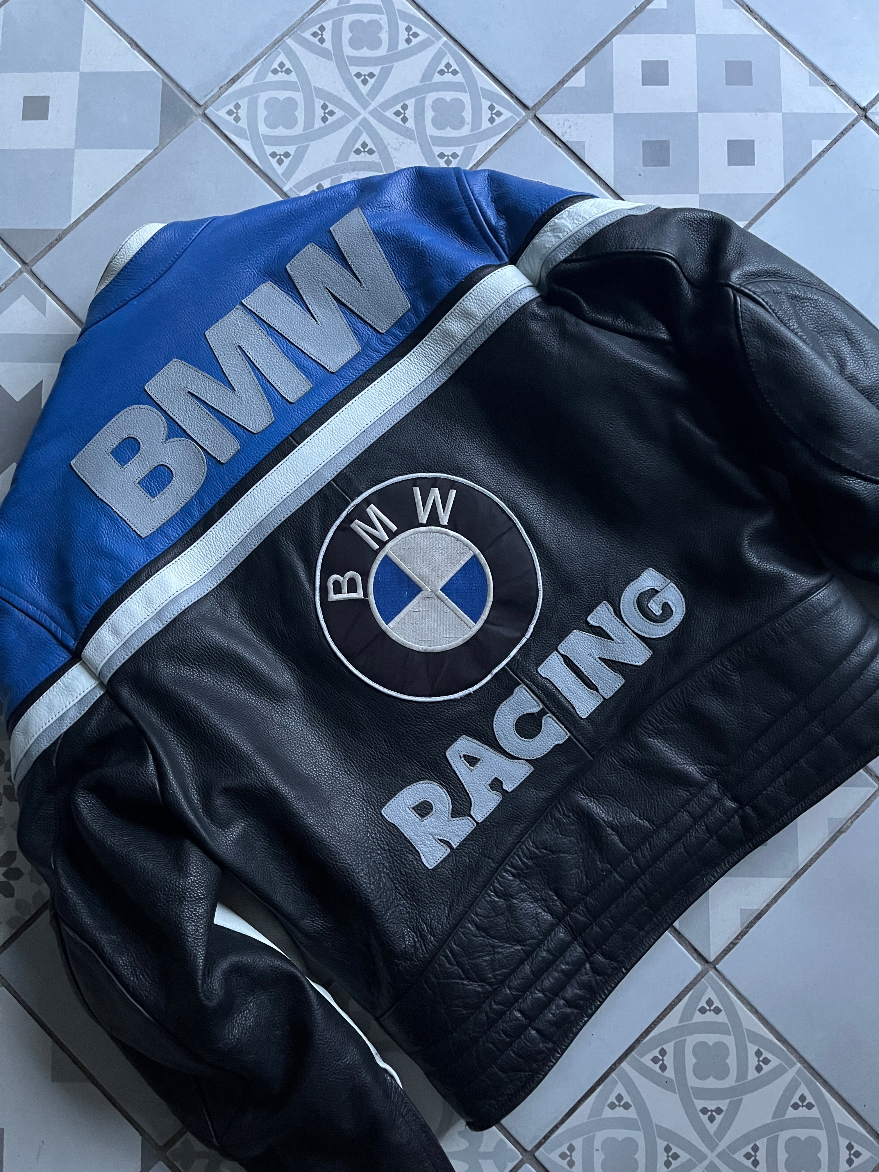 Zoom sur les détails brodés du dos : grand logo rond BMW et lettrage RACING argenté sur le cuir noir grainé.