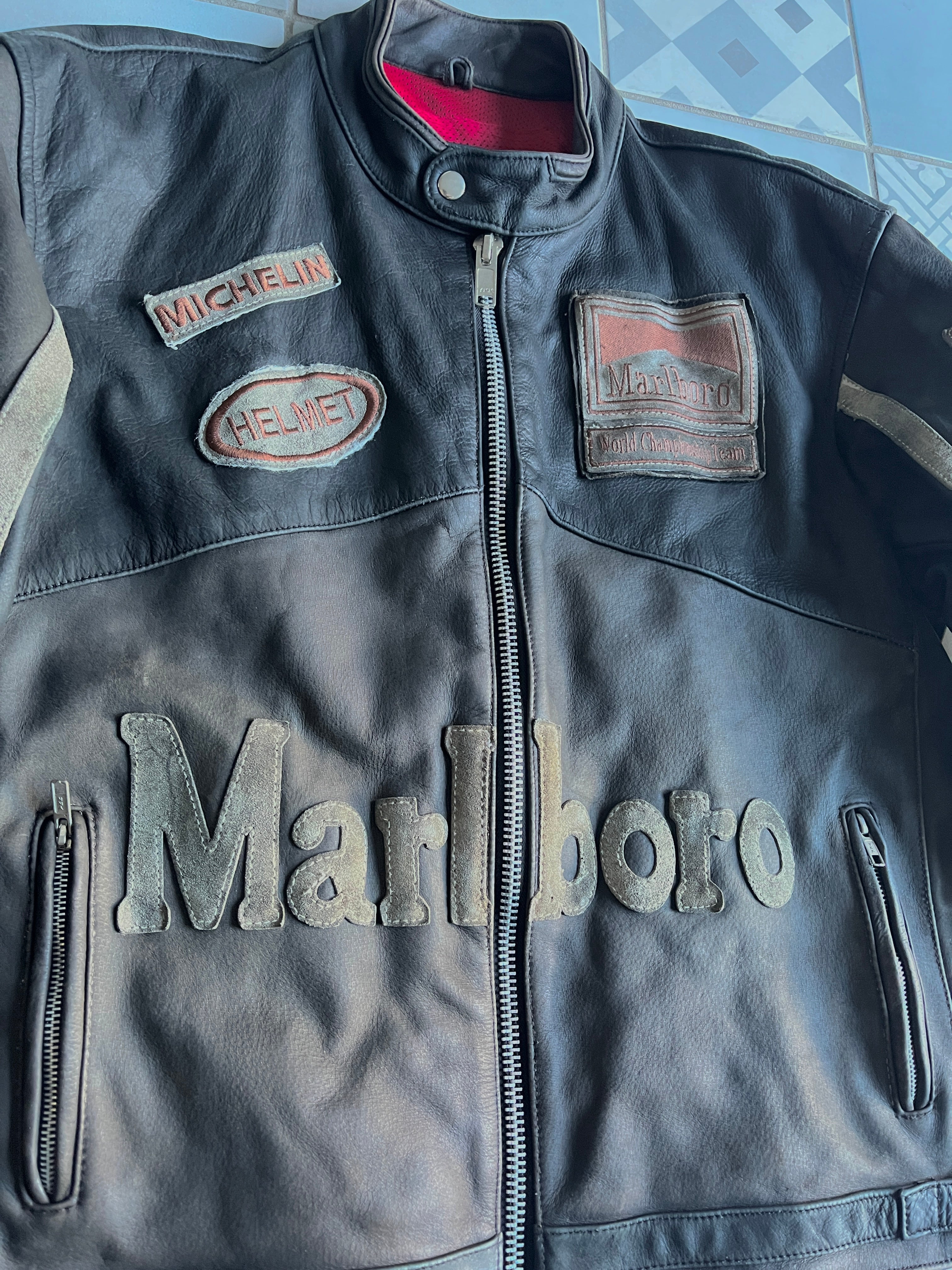 Gros plan sur la poitrine du blouson : cuir vieilli gris-noir, patchs Michelin et Helmet, et lettrage Marlboro en cuir découpé