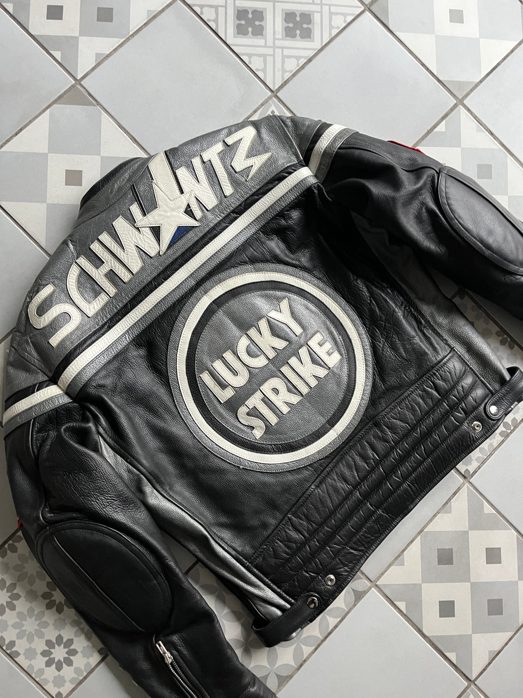 Vue de dos en biais mettant en valeur les renforts d'épaules argentés et la typographie Schwantz brodée