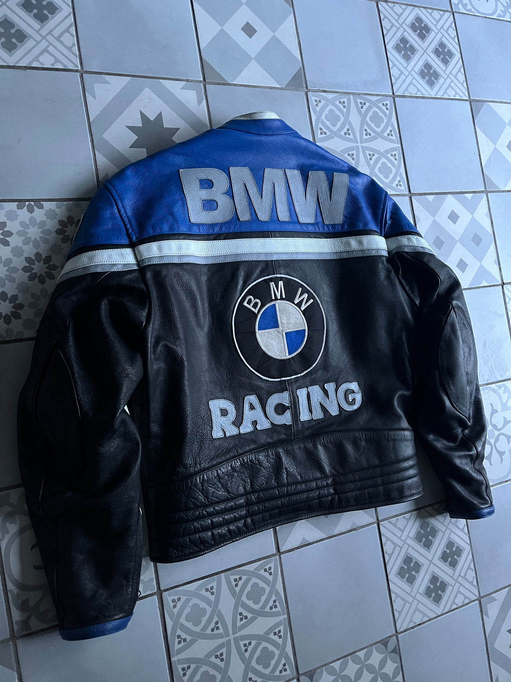 Vue arrière de biais du blouson motard BMW, montrant les renforts d'épaules et le design colorblock bleu et noir iconique.
