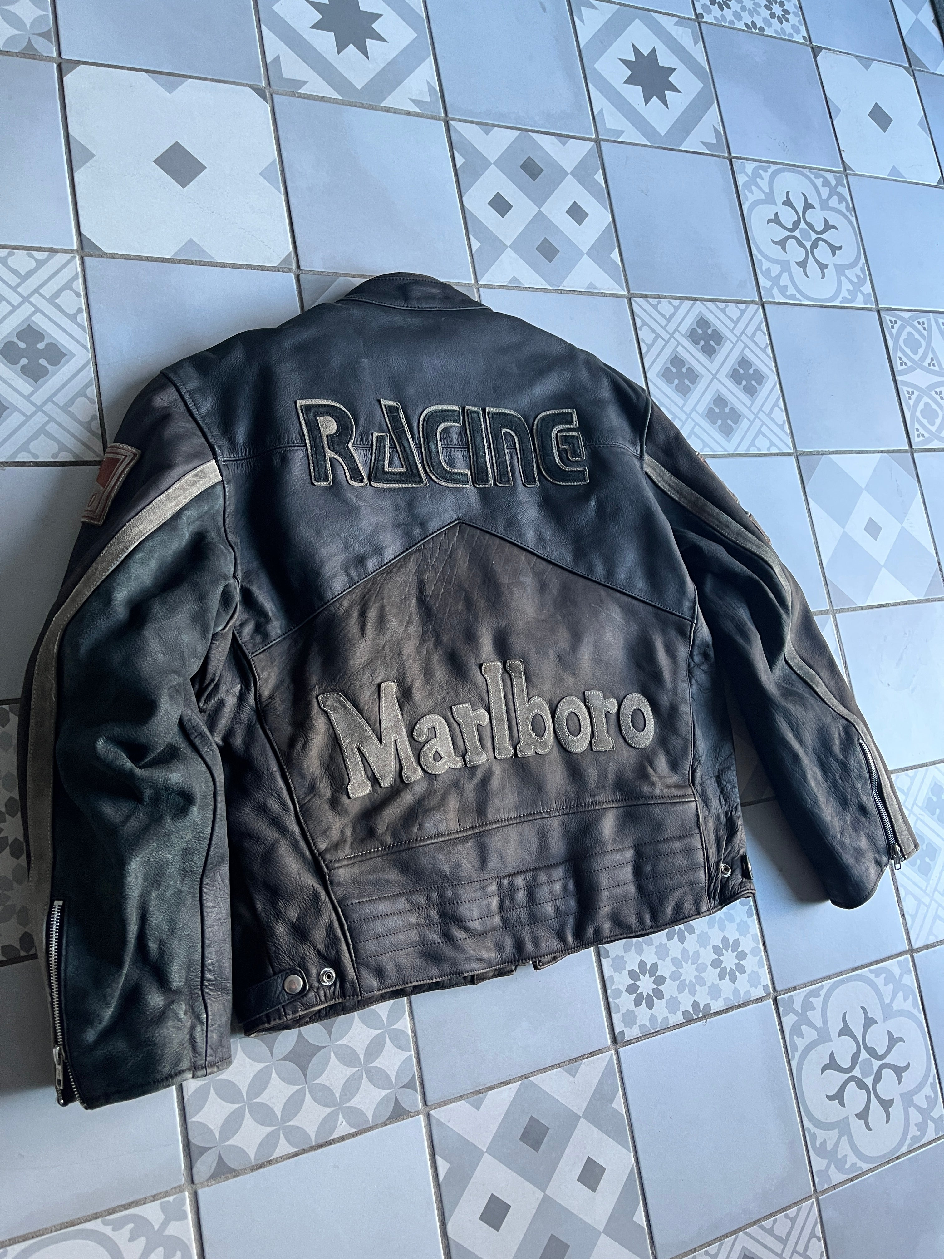 Vue arrière de biais mettant en valeur la coupe motard, la patine naturelle du cuir et le relief des logos au dos