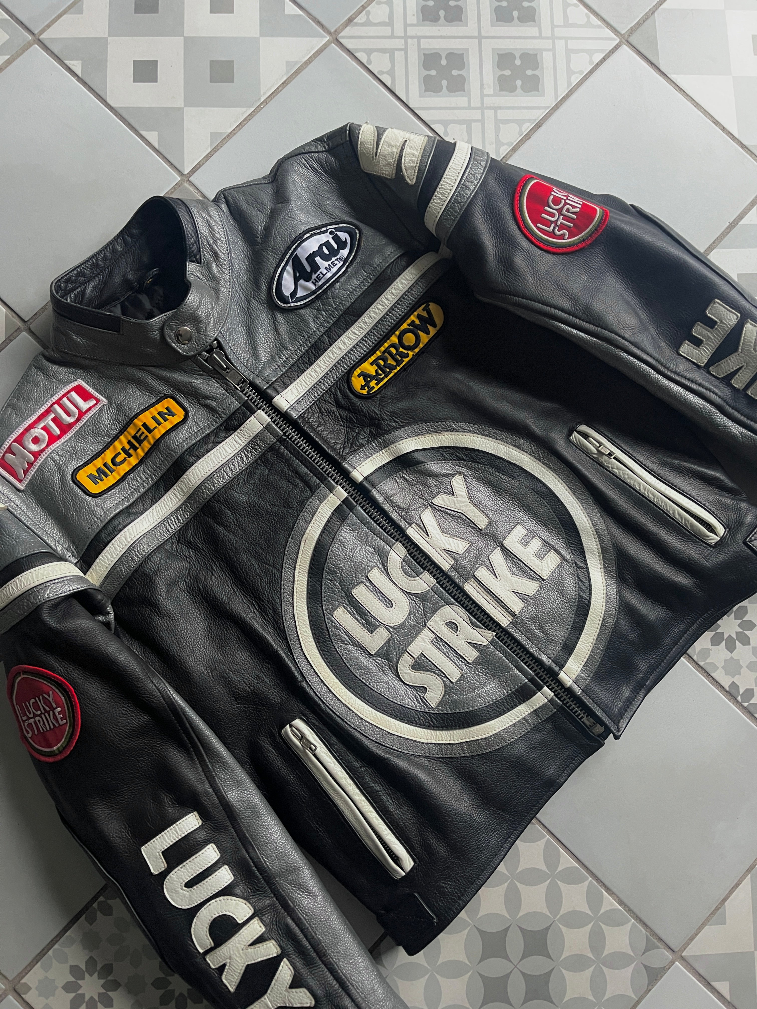 Zoom sur la poitrine : texture du cuir grainé, grand logo Lucky Strike et broderies sponsors Arai, Arrow et Michelin